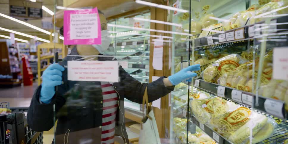 A woman with mask and gloves shopping for bread in a grocery store