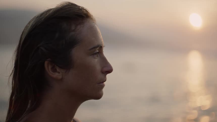 Side profile of female surfer with brown hair on the coast at sunset