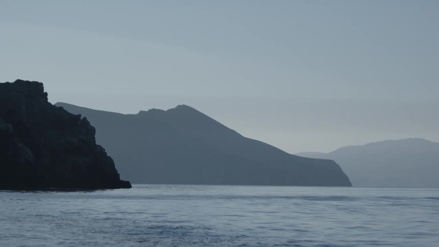 Mountains under light mist meeting with the calm ocean waters at morning