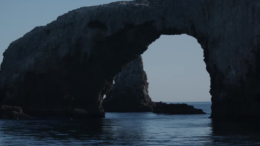 An ocean cave formation with a clear sky and ripples in the water flowing under it