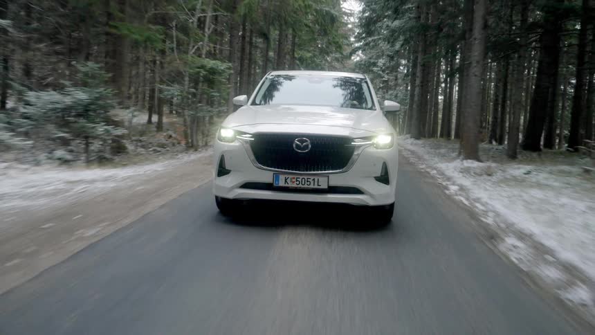 White sedan drives through snowy conifer forest