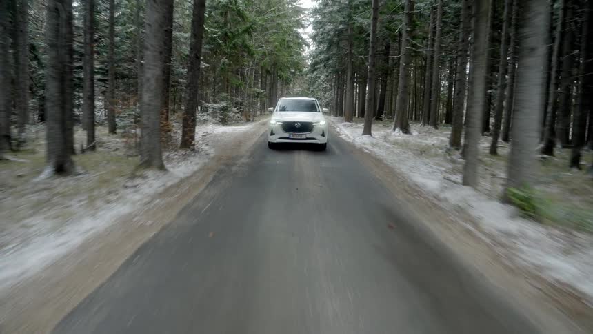 A time lapse of a white suv driving on a road through a pine forest that has a dusting of snow on the ground