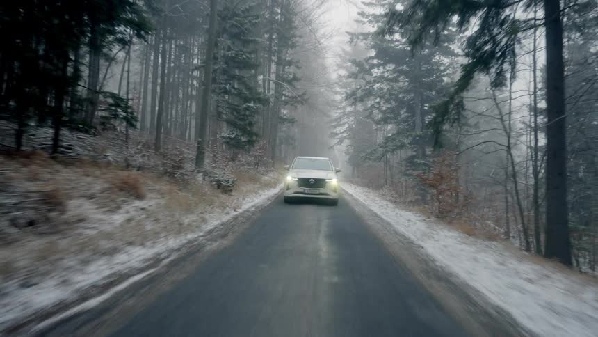 A white car flashes the headlights as it travels on a forest road on a snowy winter day