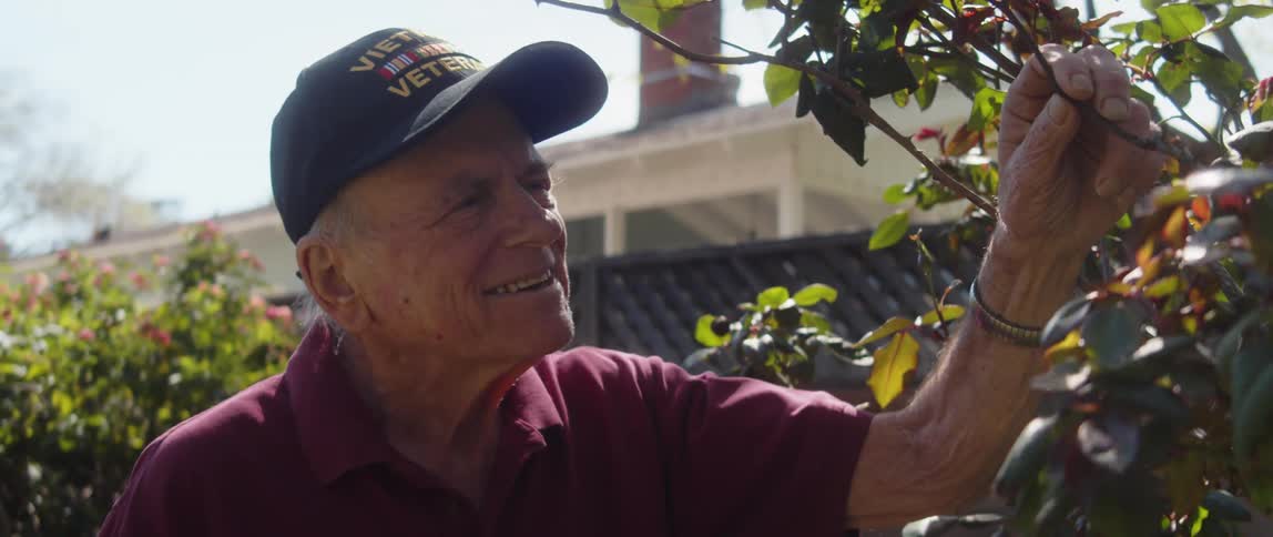 An older man outdoors looking at plants during the day light