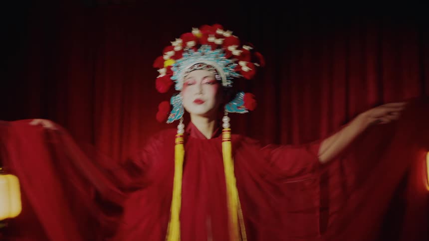 Actress on stage performing a chinese theatre dance in front of a red curtain