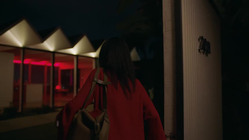 A young woman visits a hotel room at night and goes through the door to a strange lighted room