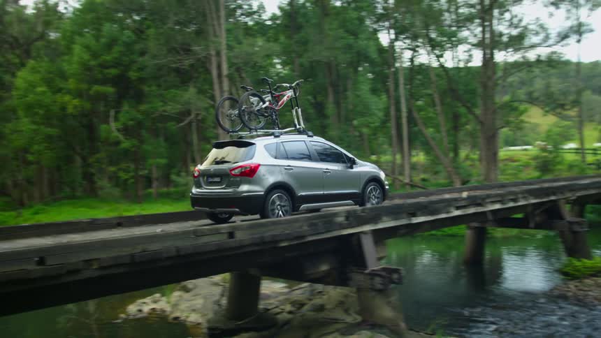 Hatchback with bicycles in a roof rack crosses bridge over stream while driving through countryside