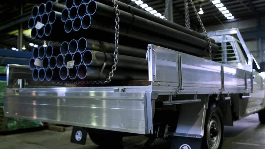 A flat bed truck and pipes being lowered onto it by chains