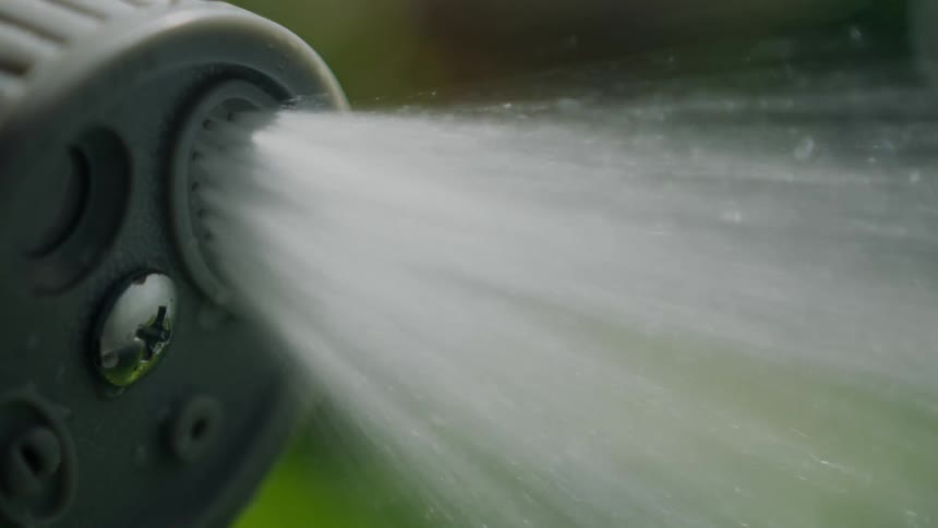 Water sprays from a hose nozzle outdoors during the day