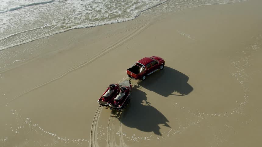 A truck is hauling jet skis on the beach