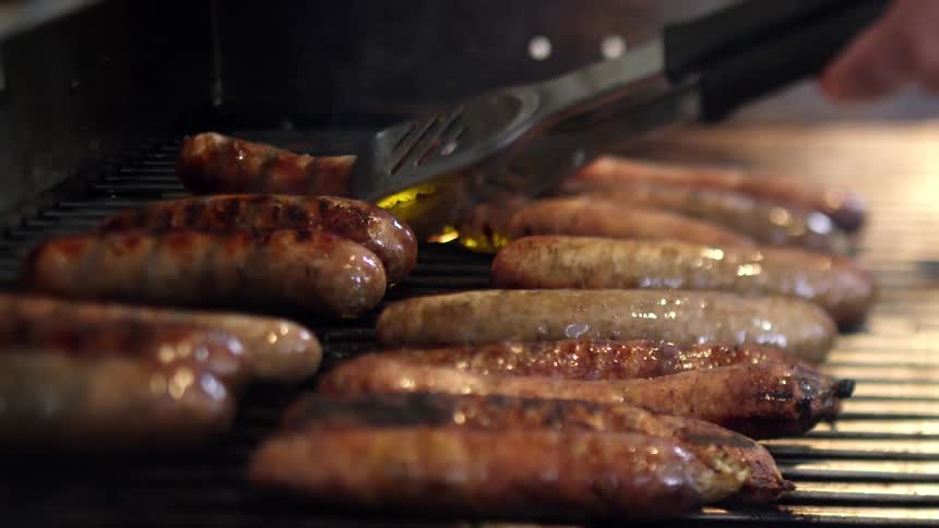 Man uses tongs to turn sausages being cooked on grill