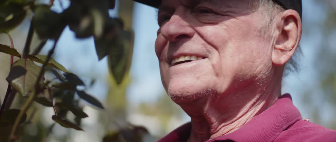 A man is smelling leaves on a branch outside