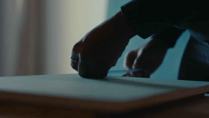 A person in a classroom standing over a table and measuring the angles and sides of a peace of wood
