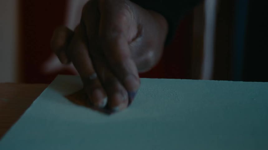 Carpenter sands the surface of a plank of wood in the dimly lit workshop