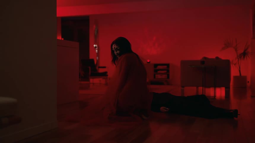 A person sitting in a dark room looking back with painting on her face hovering over a person on the floor