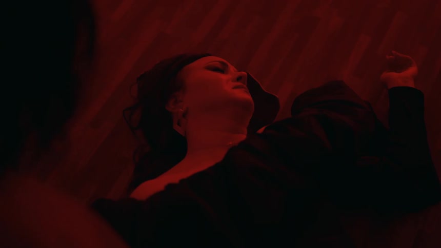 Close up of a woman wearing a black dress laying in the ground in discomfort under red lights