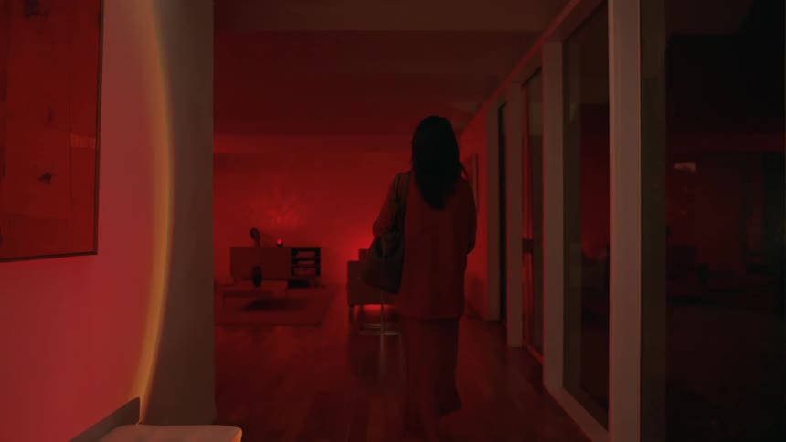 Woman wearing a black dress guides a friend through her house under red lights