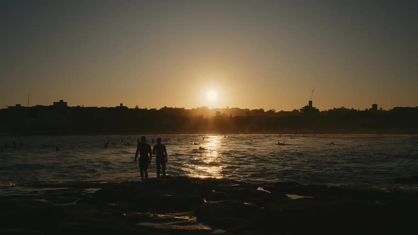 Two people stand in front of a lake watching the sun set