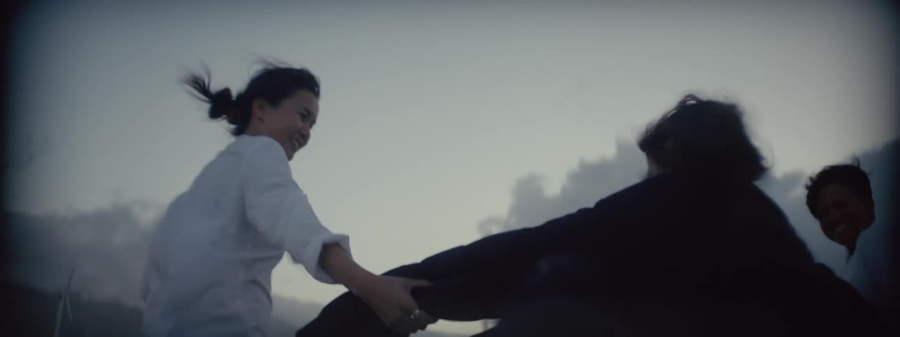 Two women wearing white shirts help another to stand on a road against a strong gust of wind