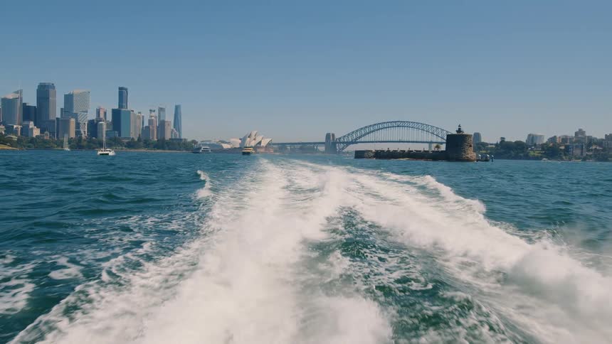View from back of boat showing wake of ferry and sydney harbour with skyline on a beautiful day
