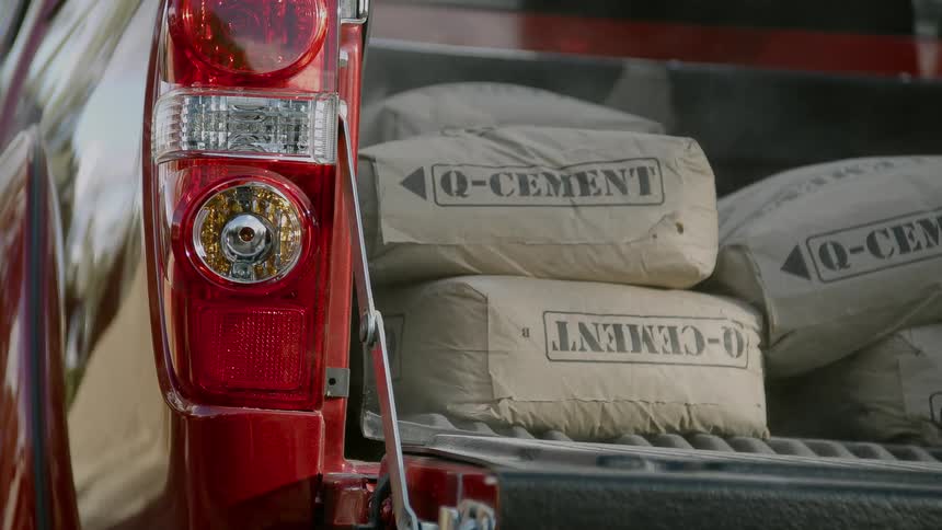 Bags of cement are falling into the back of a red pickup truck