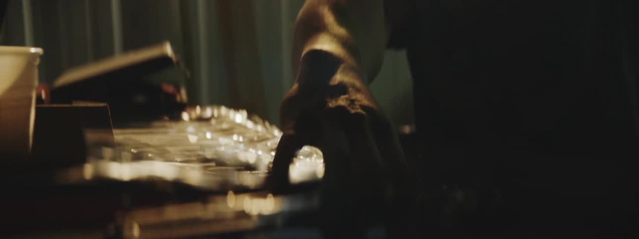 Silhouette of a man working in a dark workshop picking up tools from a table