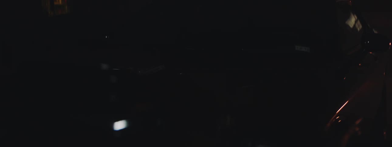 A dark colored car hood reflecting light off it and shadows from the ceiling