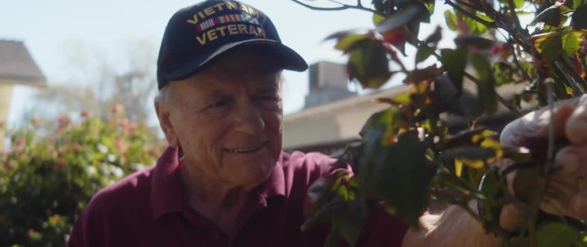 Man with dark blue cap and crimson shirt gardens in the backyard of house