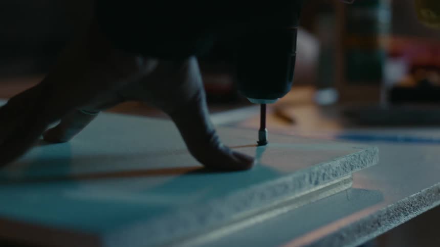 Woman uses drill to attach boards together while constructing furniture