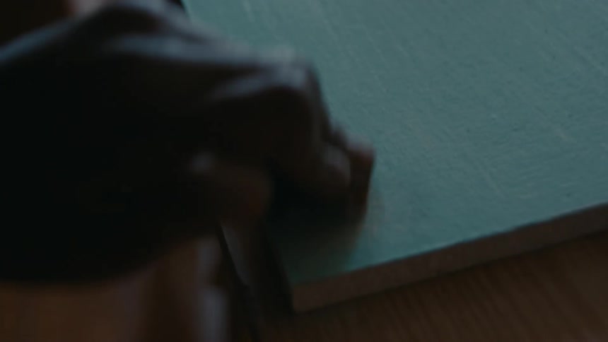 Close up of the hands of a carpenter sanding the corner of a painted plank of wood
