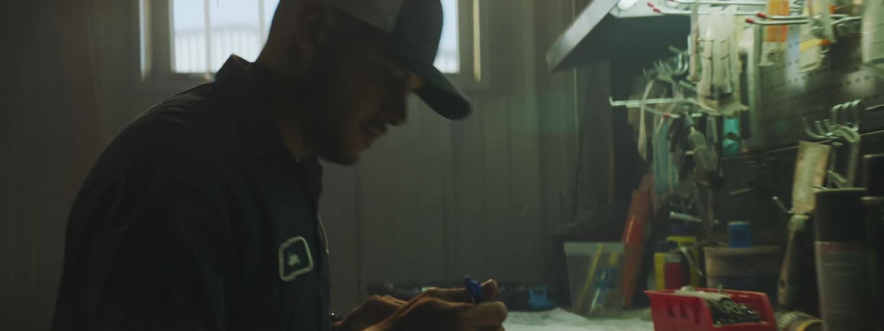 A man sitting at a work bench writing on paper under a work light
