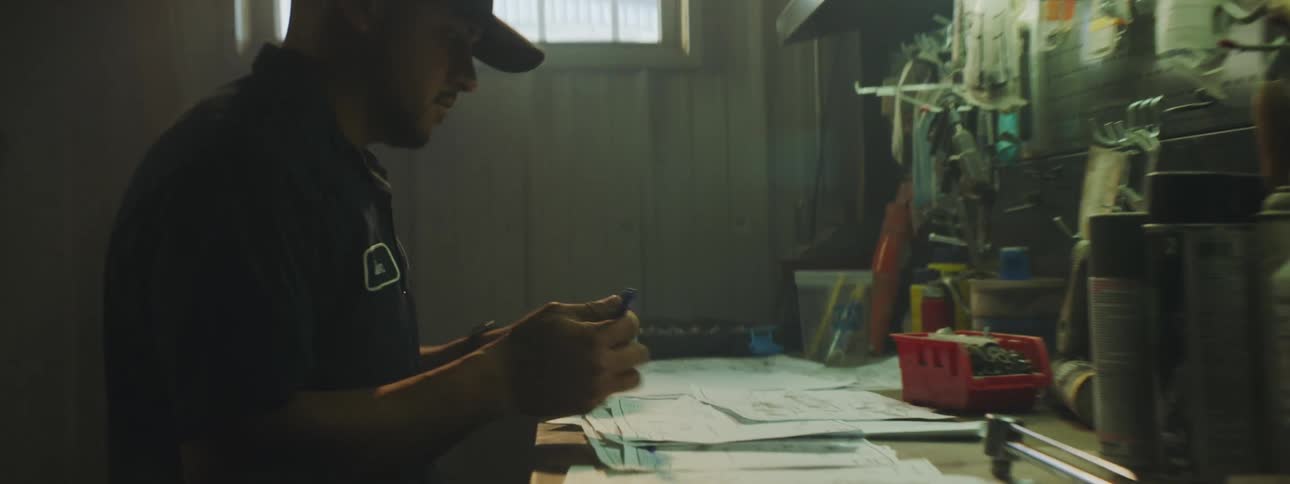 Uniformed worker in garage turns to workbench to make notes