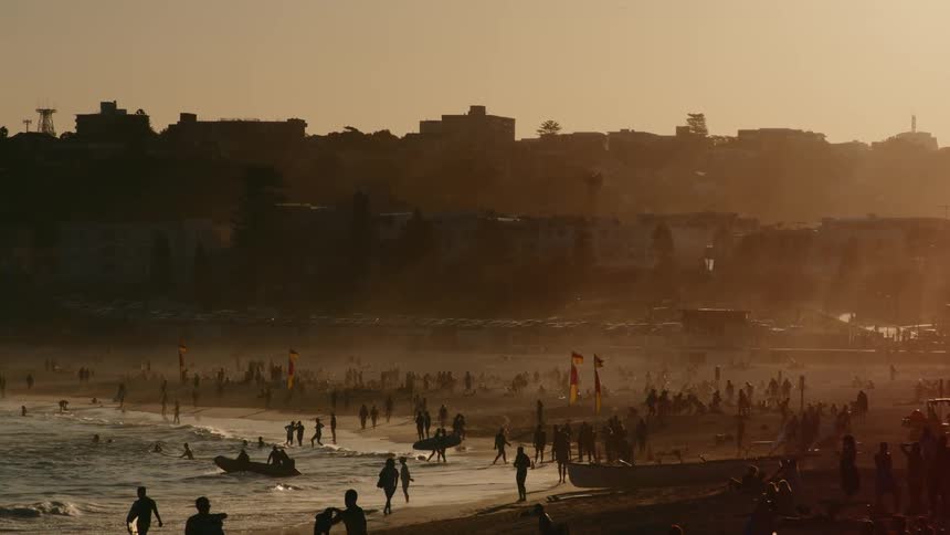 A large crowd of people on the beach and coastal city at sunset