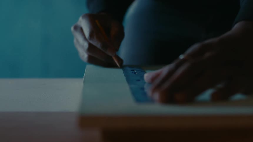 Close up of the hands of a carpenter using a ruler to mark measurements on a plank of wood