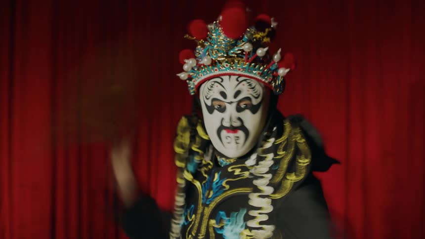 A dancer dressed in a costume and mask waving a fan around on stage