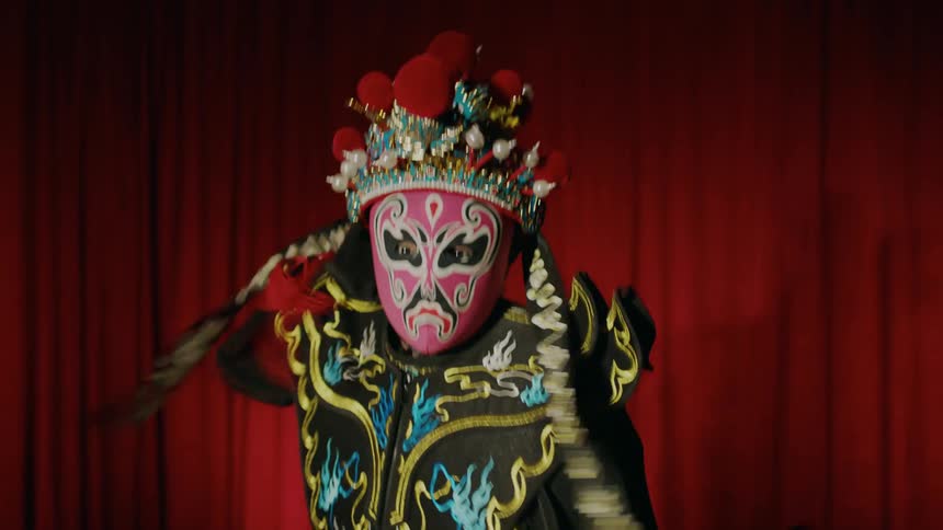 Performer wearingcostume and mask that changes color performs on stage against a red curtain