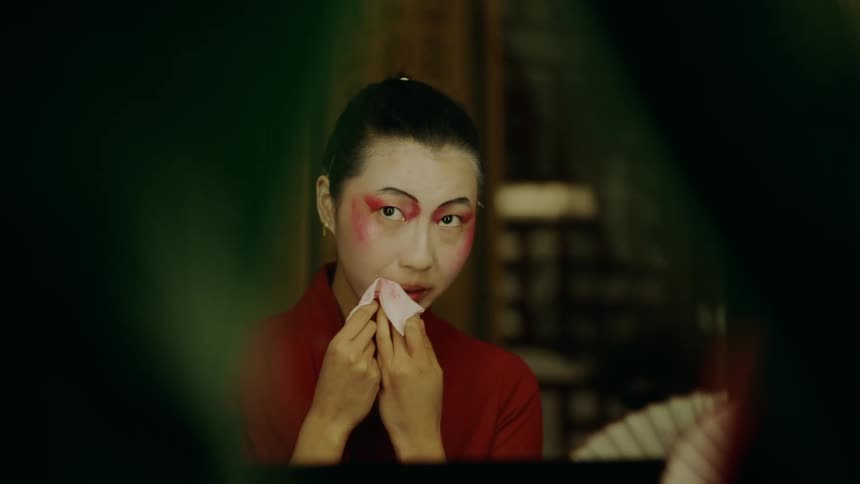 Actress sitting on a dressing room applies makeup for a chinese theatre performance