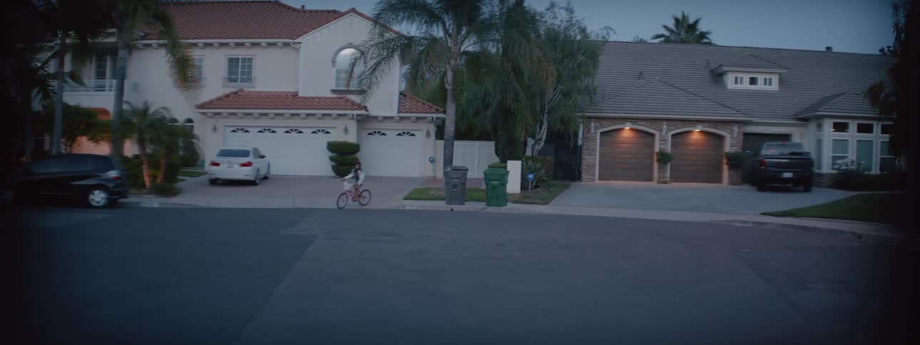 Girl rides her bicycle around the garbage bins in front of houses on the suburbs