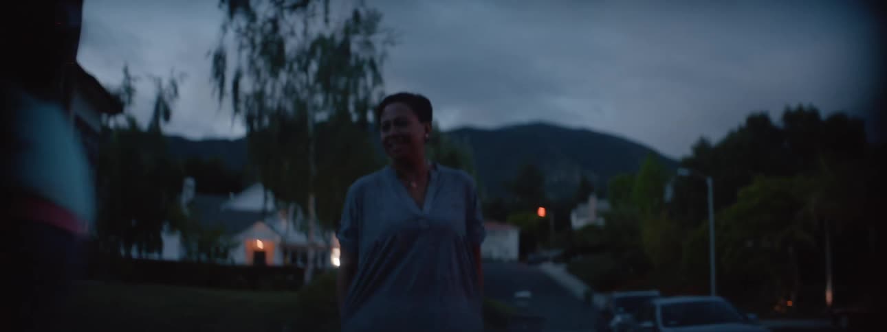 Woman watches girl riding a bicycle in the neighborhood at dusk