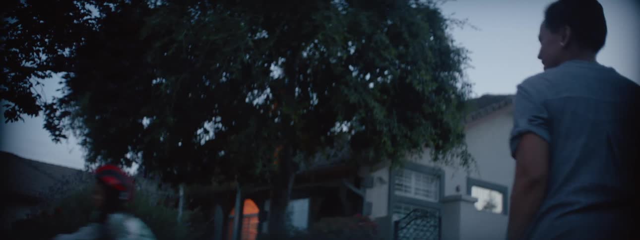 A woman watches as a girl rides a bicycle around a residential area