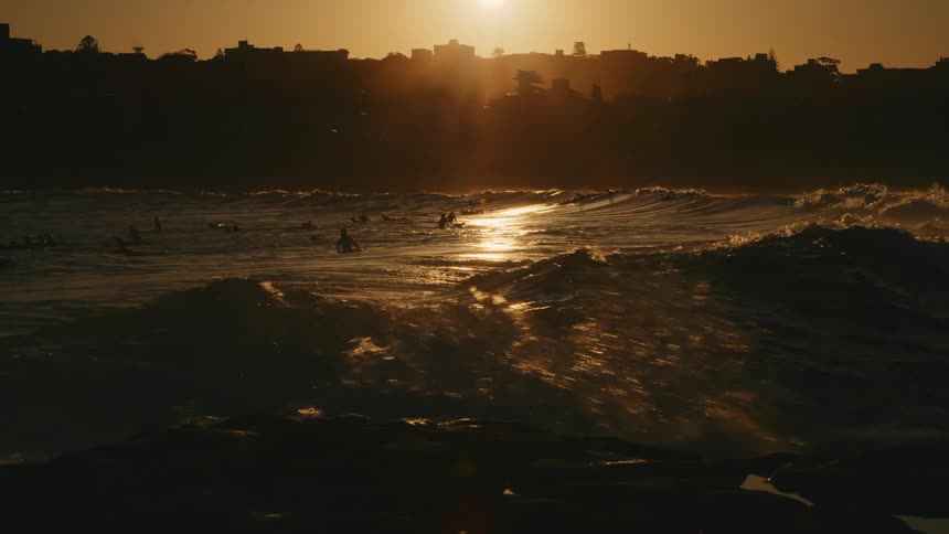 Slow motion footage of ocean waves crashing in the coast in front of the city at golden hour