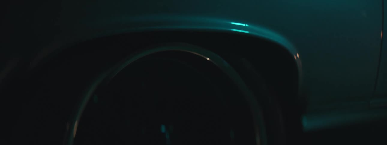 Metallic blue paint on vehicle near tire reflects light in dimly lit area