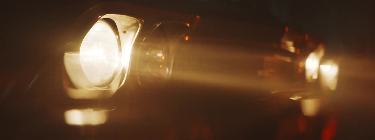 Close up of the headlights of a vintage car turned on inside a dark garage
