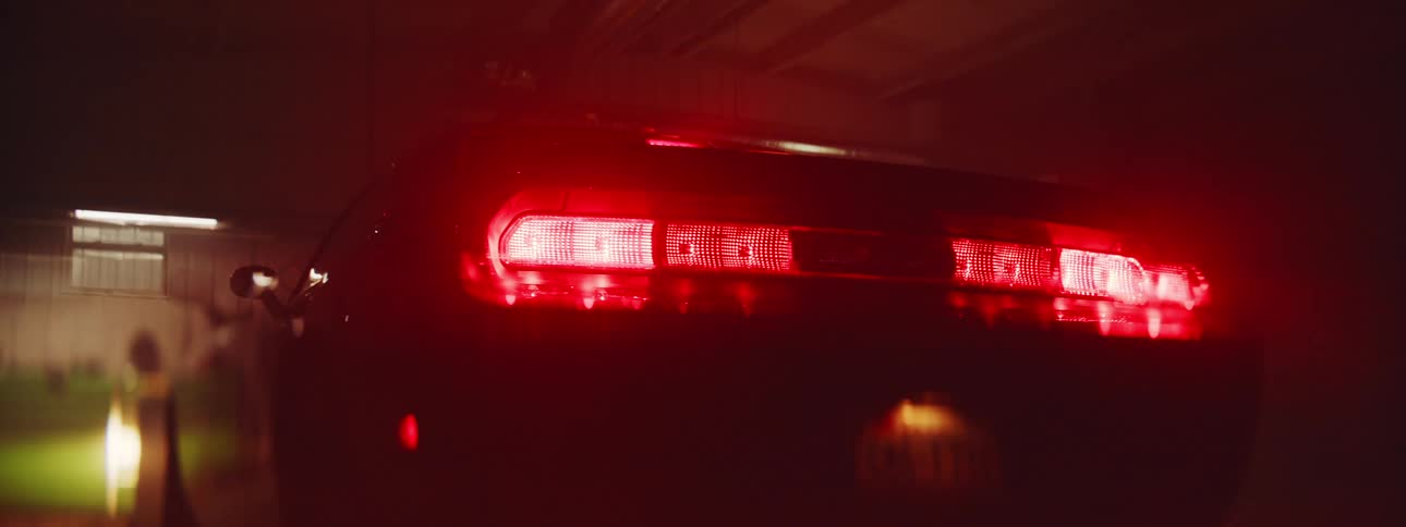 The back end of a car with the head lights in in a dark garage with lights flashing over it