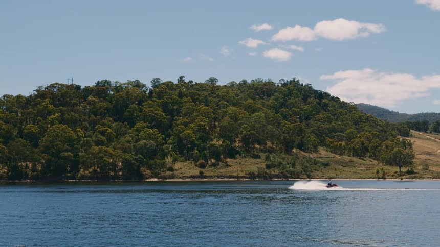 A person on a jet ski on a lake with trees on a hillside on the opposite side
