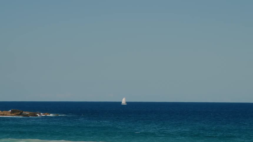 A sailboat near the horizon on the blue ocean waters in a clear day