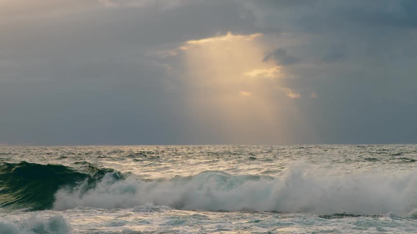 Waves crashing in the ocean as sun shines through the clouds in the landscape