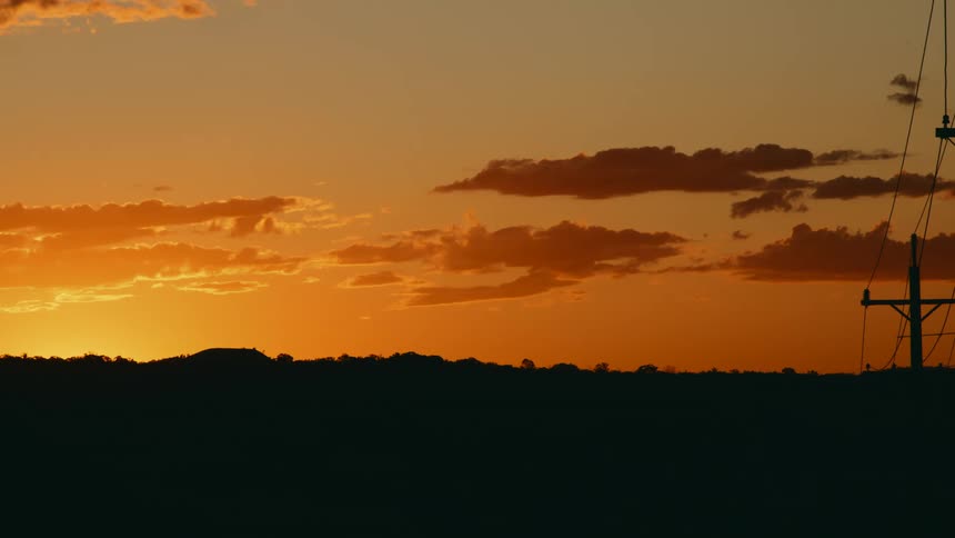 An orange and yellow sky as the sun sets with a silhouette of a tree line and power lines