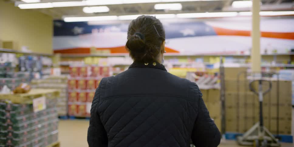 A woman with a mask pushing a shopping cart in a grocery store