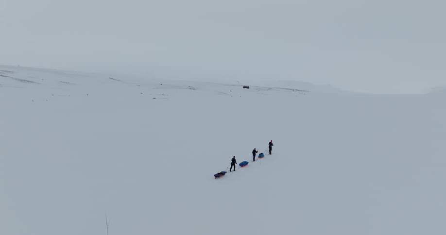 Three people are walking in a line as each person pulls a sled behind them up a snow covered hill